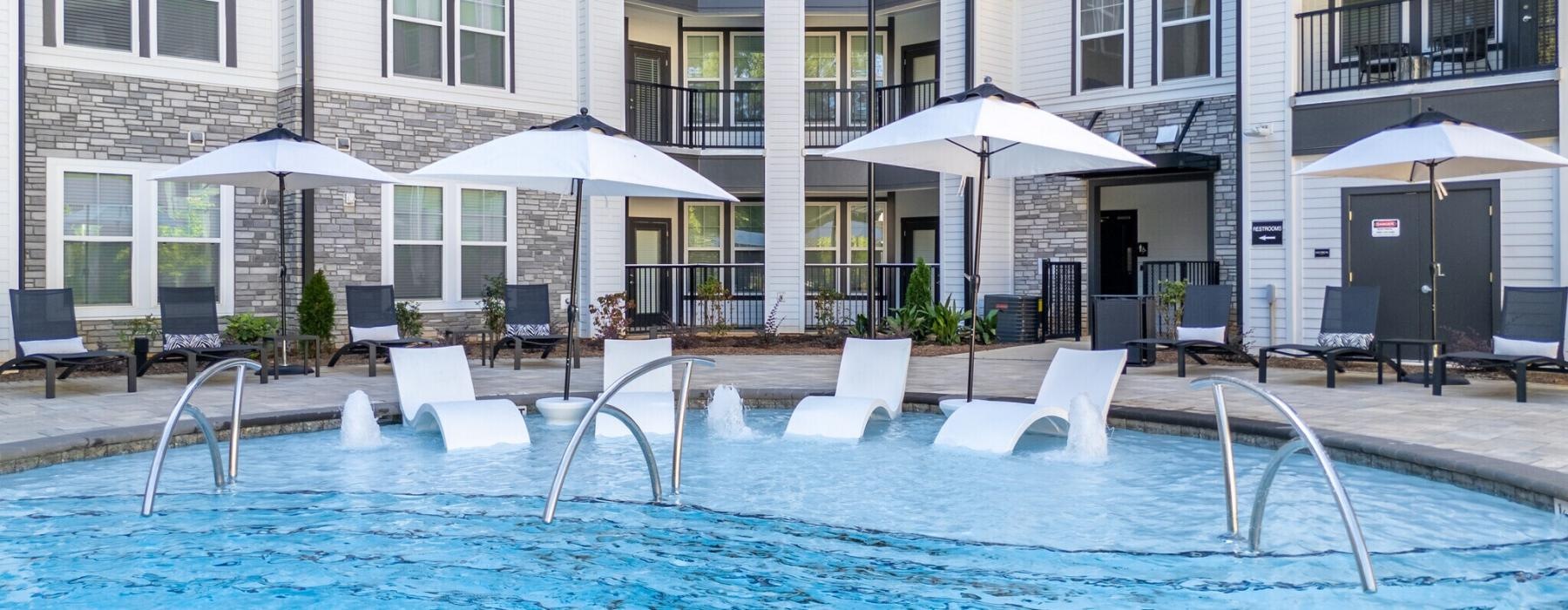 a pool with chairs and umbrellas by a building